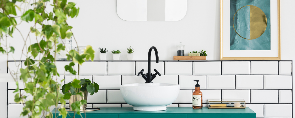 dyb hvid brugt håndvask med sort armatur i et badeværelse med en grøn plante og billede